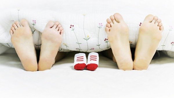 Zu sehen sind die Füße von Eltern und kleine Socken, die unter einer Bettdecke hervorschauen, um den Zusammenhang zwischen Selen, Kinderwunsch und Familie darzustellen.