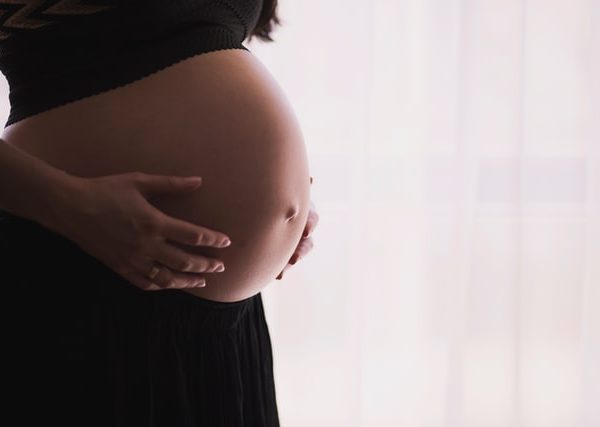 Zu sehen ist eine schwangere Frau, die schützend die Hände um ihren Bauch legt und sich informiert, welche Folgen ein Mangel an Selen in der Schwangerschaft haben kann.