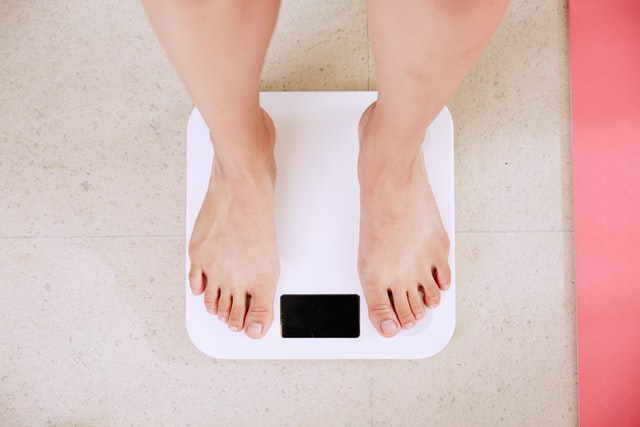 Zu sehen ist eine Frau, die auf einer Waage steht und sich fragt, ob die Einnahme von Selen bei der Gewichtsabnahme helfen könnte.